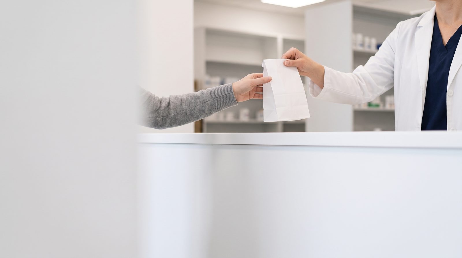 A pharmacist hands a patient a bagged prescription across the pharmacy counter
